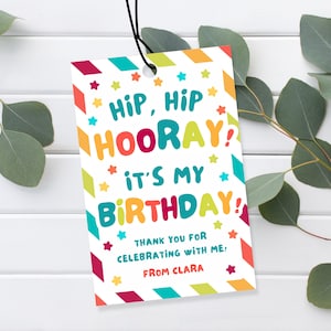 Puede incluir: Una colorida etiqueta de regalo de cumpleaños con el texto "HIP, HIP HOORAY! IT'S MY BIRTHDAY!" y "THANK YOU FOR CELEBRATING WITH ME! FROM CLARA". La etiqueta tiene un fondo blanco, una cuerda negra y está decorada con estrellas y formas geométricas.