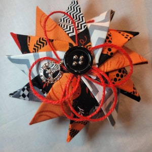 May include: A handmade orange, black, and white fabric star ornament with a black button and a silver charm. The star is tied with red twine.