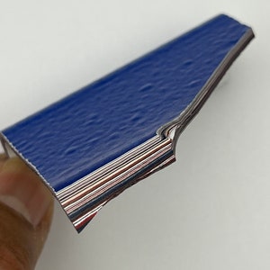 May include: A stack of blue, red and white paper with a silver edge. The paper is folded in half and the edges are visible.