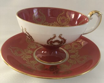 May include: A red and white teacup and saucer set with gold trim and a floral pattern. The cup has a white interior and a red exterior with gold accents. The saucer is red with gold accents and a floral pattern.