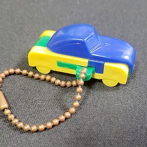 May include: A blue, yellow, and green plastic toy car keychain. The car has a rounded shape and a chain attached to the bottom.