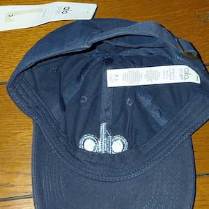 May include: A navy blue baseball cap featuring the white embroidered text alo on the front panel. The cap includes a white paper hang tag with the brand logo and an interior white fabric care label with text detailing material composition.