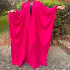 May include: A vibrant fuchsia-colored ensemble, featuring a flowing, open-front robe with wide sleeves. The robe is paired with a matching skirt or pants, creating a coordinated outfit. The outfit is made of a lightweight fabric.
