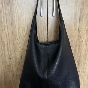 May include: A black leather shoulder bag with a textured surface hangs from a silver handle. The bag has a simple, minimalist design and a large capacity. The bag is made of a durable material and is suitable for everyday use.