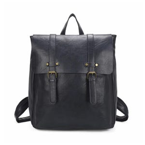May include: A black backpack with a flap closure, two buckle straps, and a top handle. The backpack has a textured appearance and brass-coloured hardware. The shoulder straps are visible on either side of the bag.