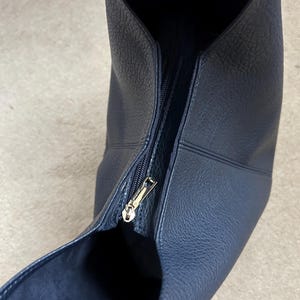 May include: A navy blue leather handbag with a gold zipper. The bag has a textured surface and a wide opening. The zipper is partially open, revealing the interior of the bag.