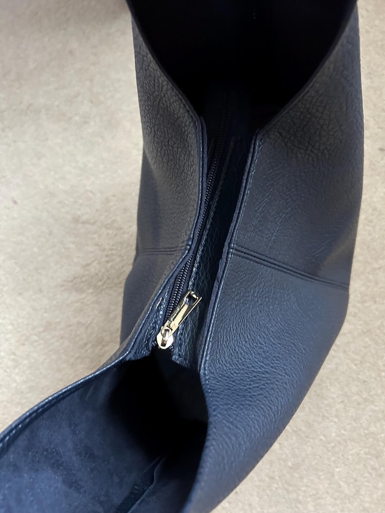 May include: A navy blue leather handbag with a gold zipper. The bag has a textured surface and a wide opening. The zipper is partially open, revealing the interior of the bag.