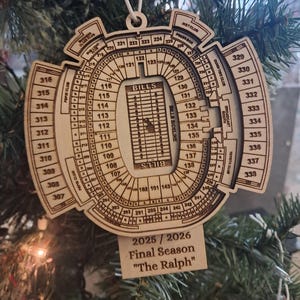 May include: Wooden ornament shaped like a stadium, with detailed seating sections and the word "BILLS" in the center. The text "2025/2026 Final Season 'The Ralph'" is displayed below. The ornament hangs from a white string.
