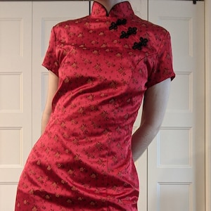 May include: A red short-sleeved dress with a floral pattern and a mandarin collar. The dress has black buttons and a fitted silhouette.