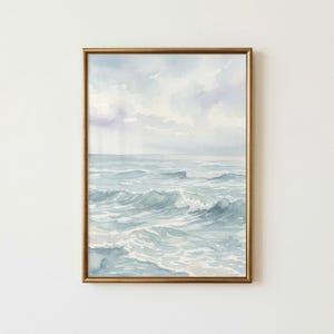 May include: A framed watercolor painting depicting a seascape with gentle ocean waves in shades of blue and grey under a soft, cloudy sky. The artwork is enclosed in a thin, metallic gold frame, showcasing fluid brushstrokes and light tones.