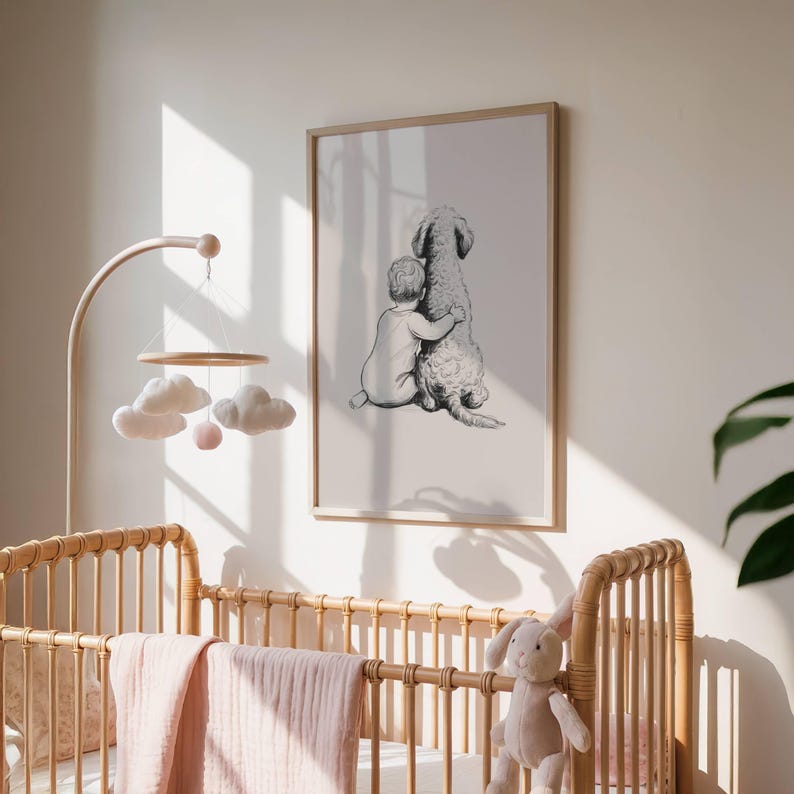 May include: A framed black and white print depicts a child embracing a large dog. The artwork is displayed above a wicker crib with a pink blanket and a mobile with cloud and ball ornaments. A stuffed bunny sits on the crib.