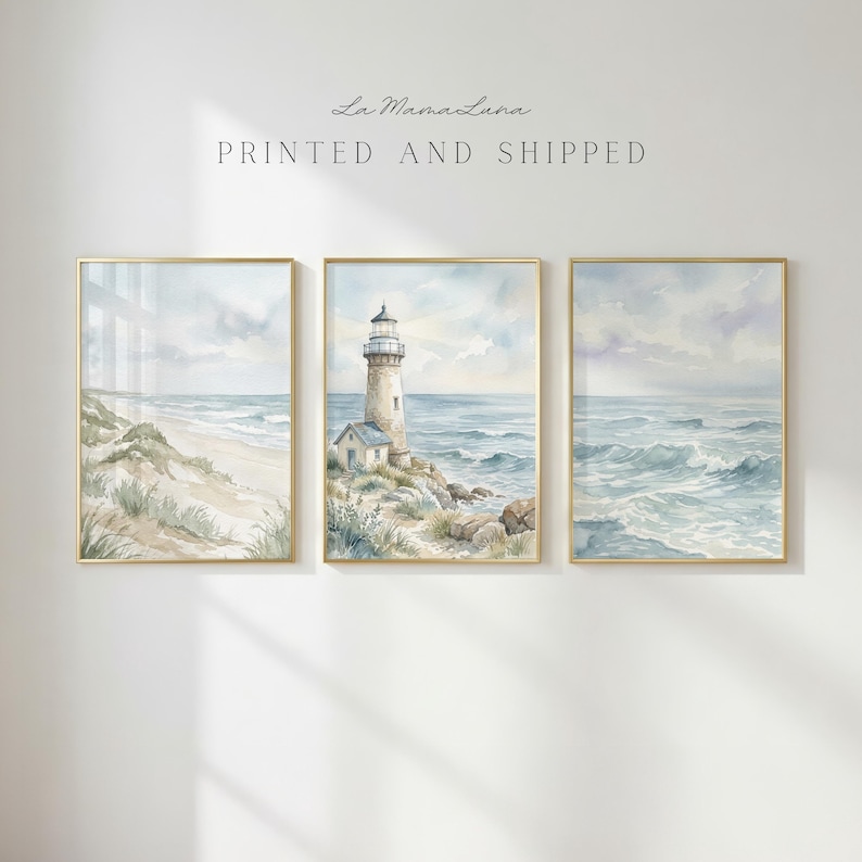 May include: A set of three framed watercolor prints featuring coastal scenes. The left print shows a sandy beach with dunes, the center print depicts a lighthouse on a rocky shore, and the right print displays ocean waves. Text reads La MamaLuna.