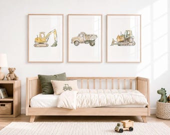 May include: Three framed watercolor prints of construction vehicles: an excavator, a dump truck, and a bulldozer. The prints are displayed above a light wood bed with a white comforter and decorative pillows. A small wooden toy truck sits on the floor.