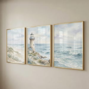 May include: A triptych of watercolor paintings in thin gold frames depicting a coastal scene. The left panel shows a sandy beach, the center panel features a lighthouse on a rocky shore, and the right panel displays ocean waves under a cloudy sky.