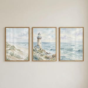 May include: A set of three rectangular wall art prints in light wood frames. The left print shows a sandy beach with dunes, the center print features a lighthouse on a rocky coast, and the right print depicts ocean waves under a cloudy sky.