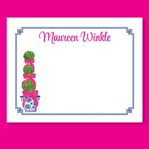 May include: White stationery with a navy blue border and the name "Maureen Winkle" in pink script. A watercolor illustration of a topiary with pink bows and a blue and white planter is on the left. The background is bright pink.