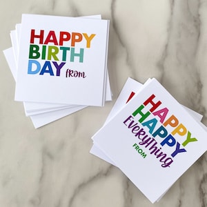 May include: Two white cards with rainbow lettering. The first card says "Happy Birthday from". The second card says "Happy Everything from".