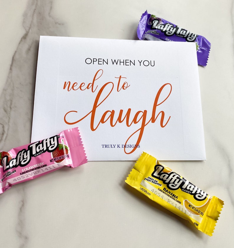 May include: A white card with the text "OPEN WHEN YOU need to laugh" in orange lettering. The card is surrounded by three Laffy Taffy candy wrappers in pink, yellow, and purple. The text "TRULY K DESIGNS" is printed in black at the bottom of the card.
