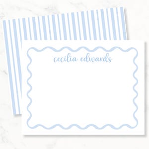 May include: A white rectangular stationery card featuring a light blue scalloped border and the name cecilia edwards printed in light blue script. The card is paired with a matching envelope that has a light blue and white vertical stripe pattern.