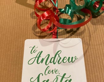 May include: A wrapped present with red and green curling ribbon and a white tag. The tag says "to Andrew love, Santa" in green script. The gift is wrapped in brown paper.