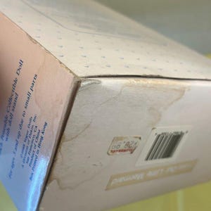 Puede incluir: Una caja de mu&ntilde;eca coleccionable vintage, con el texto "Our Little Mermaid". La caja es de color blanquecino con un patr&oacute;n de puntos azul claro. La caja tiene una etiqueta de precio y un c&oacute;digo de barras. La caja est&aacute; ligeramente da&ntilde;ada.