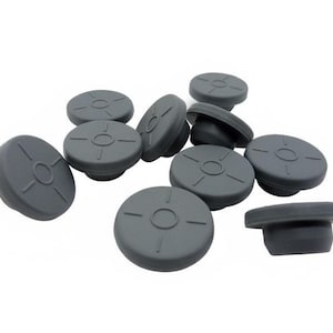 Puede incluir: Un conjunto de tapones de botella de goma gris. Cada tapón tiene una parte superior circular con un diseño empotrado que presenta un círculo central y cuatro líneas radiales. Los tapones están diseñados para encajar perfectamente en las botellas.