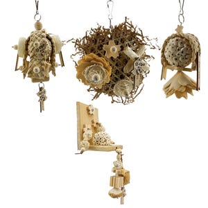 Può includere: Una collezione di giocattoli per uccelli, tra cui una figura di paglia intrecciata, una palla di carta sminuzzata con accenti floreali, una mensola di legno con elementi sospesi e una palla con perline di legno. Ogni giocattolo è sospeso da un gancio di metallo.