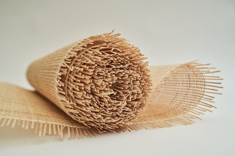 May include: A roll of natural brown woven cane webbing with fringed edges. The webbing is rolled up tightly and the fringe is visible on both ends.