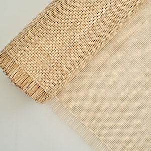 May include: A roll of natural cane webbing, a woven material used for chair seats and other furniture projects. The webbing is beige in colour and has a fringed edge.