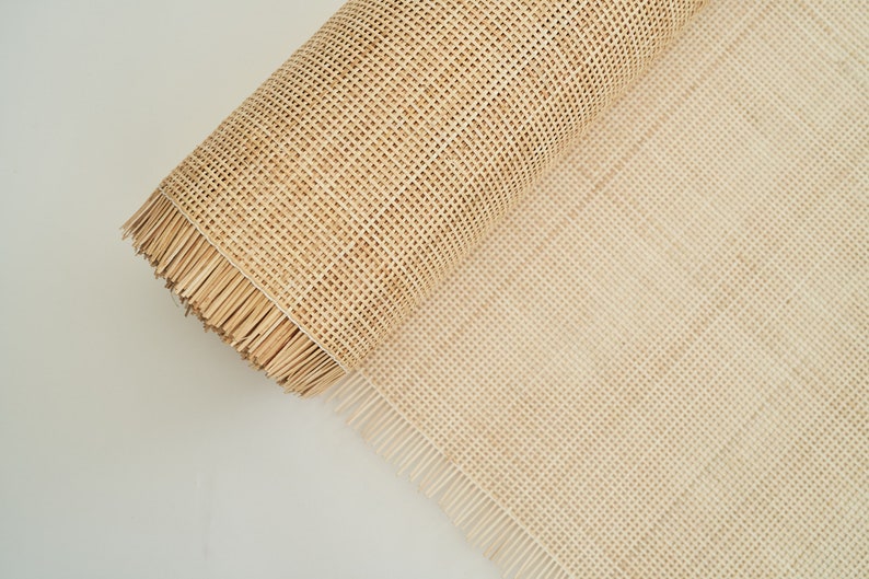 May include: A roll of natural cane webbing, a woven material used for chair seats and other furniture projects. The webbing is beige in colour and has a fringed edge.