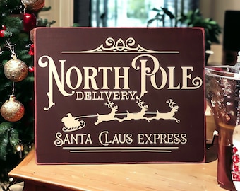 Get in the Holiday Spirit with this 8" x10" Burgundy Wood Canvas Sign with Ivory 'North Pole Delivery' Lettering