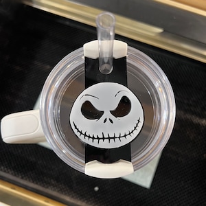 May include: A white tumbler with a black lid and a black and white Jack Skellington design. The tumbler has a straw.