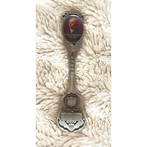 May include: A silver souvenir spoon featuring an oval portrait of George Washington, the text "George Washington 1st President 1789-1797", and an image of the White House. The spoon has a decorative handle and is likely a collectible item.