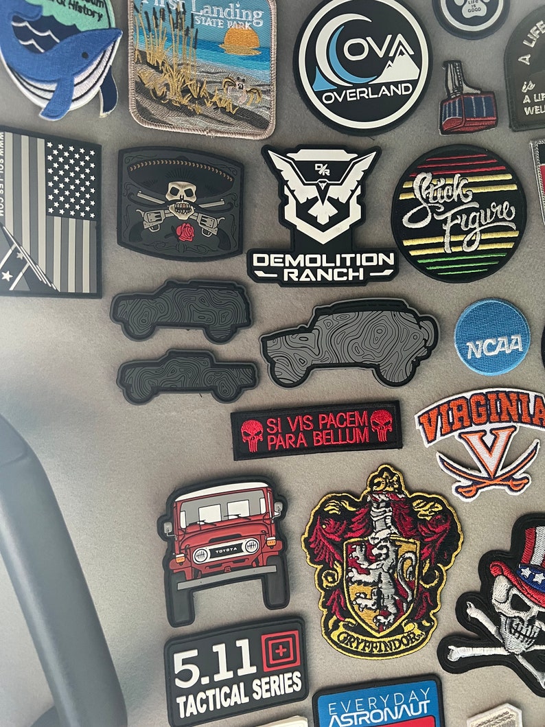 May include: A selection of embroidered patches and decals. Notable designs include a red Toyota Land Cruiser, a skull with crossed guns, and a patch with the text "Demolition Ranch". Other patches feature the text "Gryffindor" and "5.11 Tactical Series".