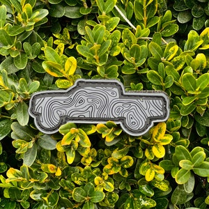 May include: A black and gray topographic map design of a pickup truck. The truck is outlined in black and filled with gray topographic lines.