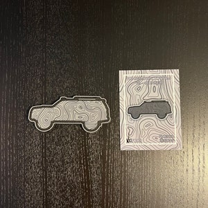 Może przedstawiać: Czarno-biała naklejka topograficzna z samochodem z tekstem "Topographic Toyotas V2 - 4Runner" i "100 x 100" nadrukowanym na naklejce.