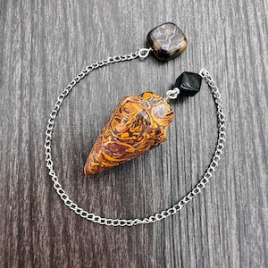 May include: A brown and orange marbled crystal pendulum with a silver chain and black and brown crystal accents.