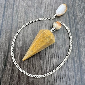 May include: A brown and white crystal pendulum with a silver chain. The pendulum is hanging from a wooden surface.