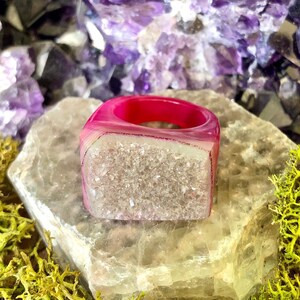Può includere: Un anello in agata rosa con un centro di cristallo trasparente. L'anello è realizzato in pietra naturale e ha una forma unica e organica.