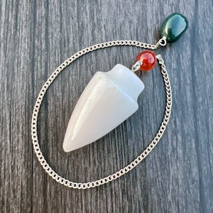 Puede incluir: Pendulo de cristal blanco con una cadena plateada y detalles de piedras preciosas rojas y verdes.