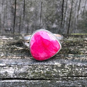 May include: A silver ring with a large, faceted, pink gemstone. The ring is set on a wooden surface.