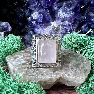 May include: A silver ring featuring a square, clear, pink quartz stone set in a filigree design.