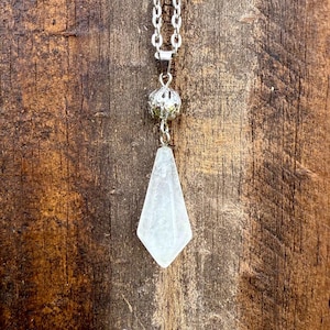 May include: A silver chain necklace with a clear crystal pendant shaped like a teardrop. The pendant is attached to a silver ball with an intricate design.