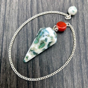 May include: A white, green, and red crystal pendulum with a silver chain. The pendulum is a pointed, teardrop shape.