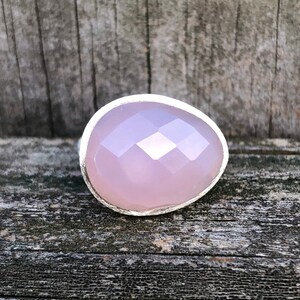 May include: A silver ring with a large, faceted, light pink gemstone. The ring is set on a wooden surface.