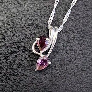 May include: A silver necklace with a pendant featuring two teardrop-shaped purple gemstones.
