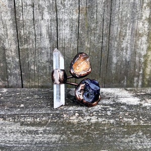 May include: A copper ring with three crystal stones. The stones are clear quartz, citrine, and amethyst. The ring is handmade and unique.