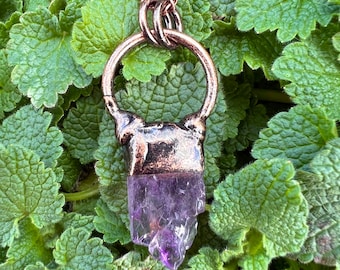 May include: A copper pendant with a purple amethyst crystal. The pendant has a ring at the top for attaching a chain.