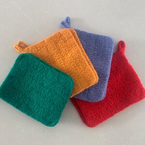 Puede incluir: Cuatro agarraderas de olla de punto en diferentes colores: verde, naranja, morado y rojo. Las agarraderas están hechas de un material suave y peludo y tienen un asa de bucle.