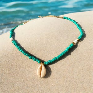 Puede incluir: Un collar de cuentas turquesa y blancas con una cadena dorada y un colgante de concha blanca.